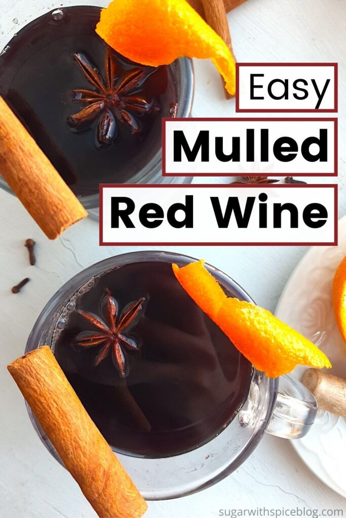 Mulled Red Wine in two clear glass mugs garnished with orange twists, star anise, and cinnamon sticks. Fresh ginger root and orange slices on a cream plate to the side. More cinnamon sticks, cardamom pods, whole cloves, and star anise scatter around on a white background. Overhead Shot. Text overlay reads easy mulled red wine with burgundy border. Pinterest image. Sugar with Spice Blog.